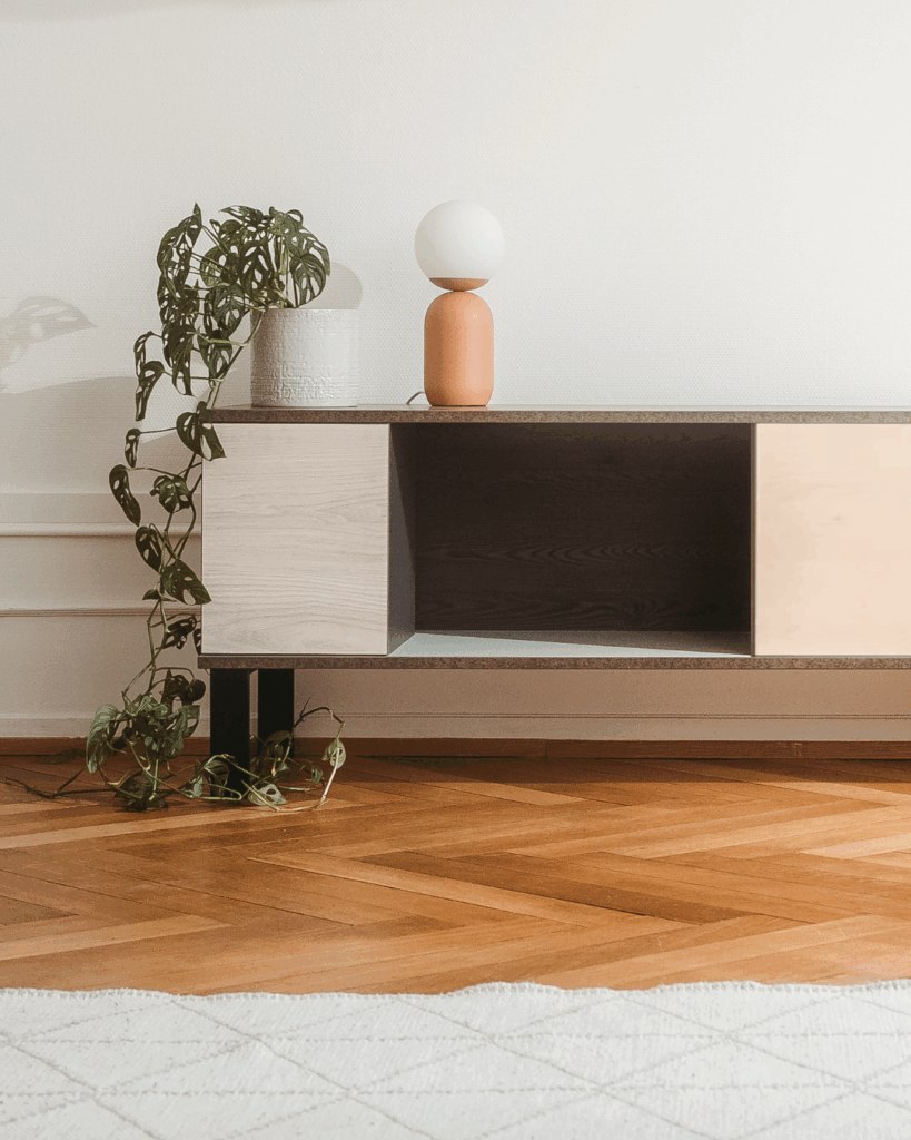 Meuble en panneaux bois revalorisés couleur claire, posé sur pieds noirs bas.