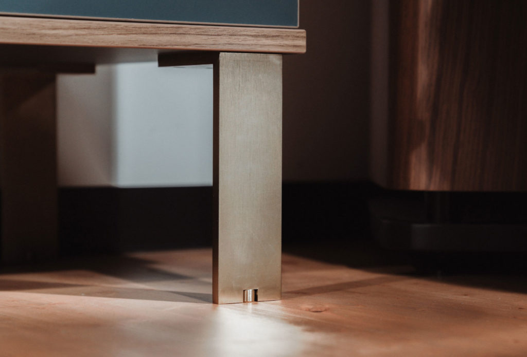 Zoom sur un pied en laiton brossé soutenant un meuble posé sur un parquet.