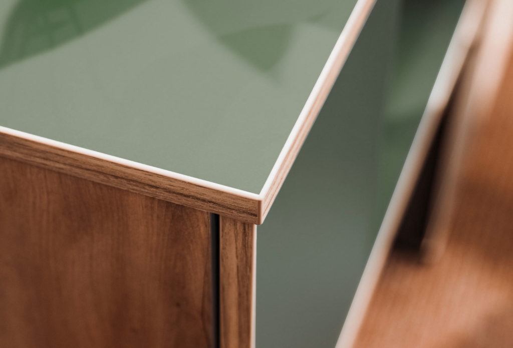 Zoom sur l’angle d’un meuble TV modulable Hecko, finition vert mat et chants en bois clair